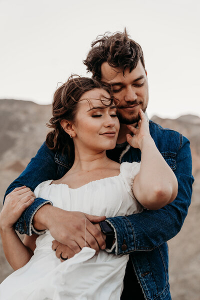 Couple embracing while the wind blows their hair at Artists Palette in Death Valley adventure photo session