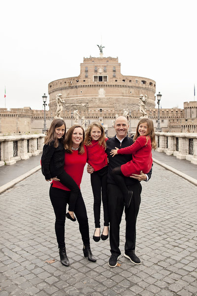 Family of five in red and black with Castel Sant'Angelo in the distance. Taken by Rome Family Photographer, Tricia Anne Photography