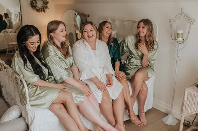 Bride and bridesmaids sitting on bed smiling in bridal suite