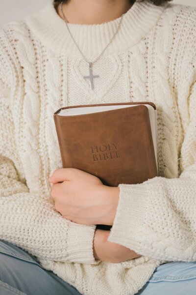 Woman wearing a sweater and holding a Bible against her chest