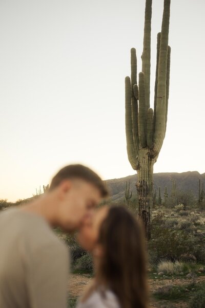 Engaged couple kissing in desert with cactus