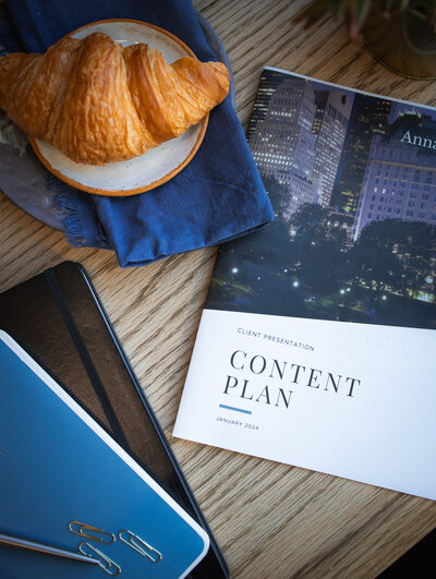 Notebooks, books about copywriting content, and a croissant laying on a table