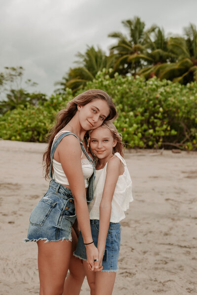 two sisters holding hands while looking at the camera on a private beach in Costa Rica with stunning views of the jungle and beach