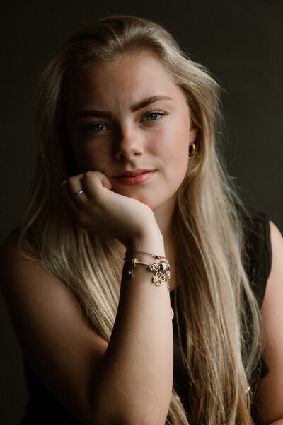 Portretfoto van jonge vrouw, haar hoofd leunt op haar hand. Gemaakt in een studio met daglicht met een donkere achtergrond. 