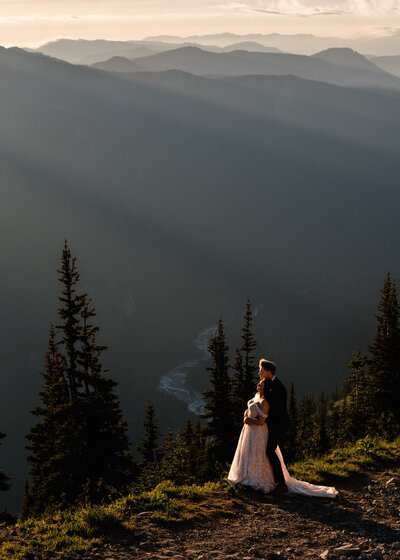 after learning how to elope in Washington State, a couple in their wedding attire embrace as they watch the sun set over the mountains