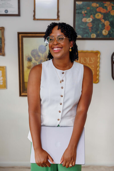 Giselle Samuels, founder of Creating Hallelujahs, smiling with a laptop in her creative studio.