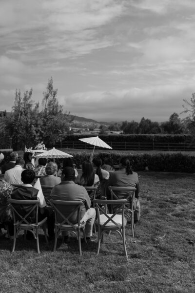 Wedding guests sitting with parasols, waiting for the ceremony to start, in black and white.