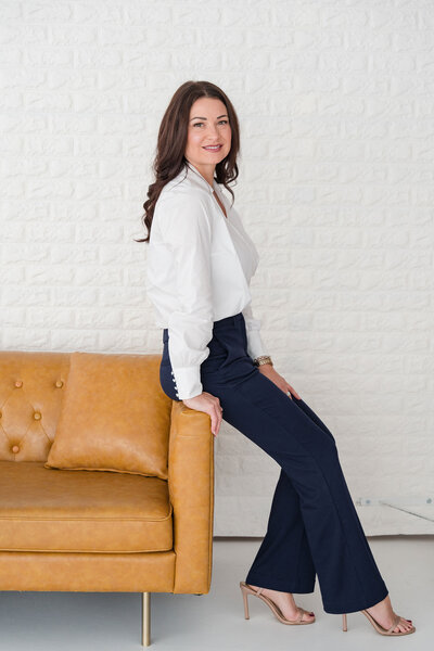 CoolSculpting consultation Dallas professional in an elegant office, sitting on a brown couch, dressed in a sophisticated outfit, ready to guide clients through the treatment process.