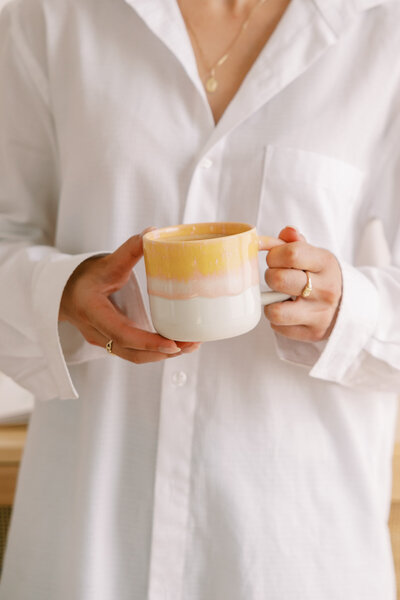 A woman wearing a white button down holding a mug of coffee 
