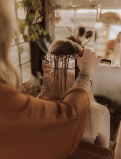 Extension services specialist is working on his client's hair. In front of them is a mirror with vintage decoration in the hair salon.