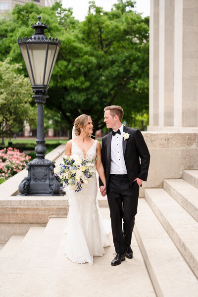 Bride and groom hold hands and smile at each other as they walk along the steps of the Ohio Statehouse