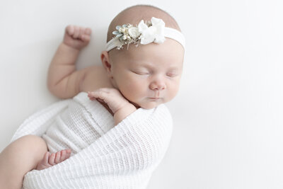 newborn baby girl with bow swaddled and sleeping