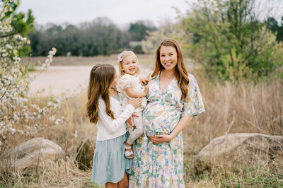 Pregnant woman in a teal dress poses with daughters for a maternity photo by Worth Capturing.
