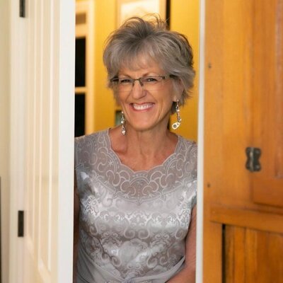 Silver haired woman wearing a silver dress smiling as she peeks through a doorway