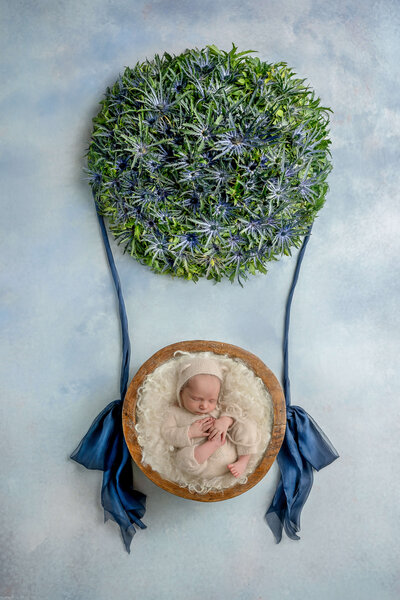 Newborn girl wearing a yellow swaddle and a yellow headband with sunflowers around her