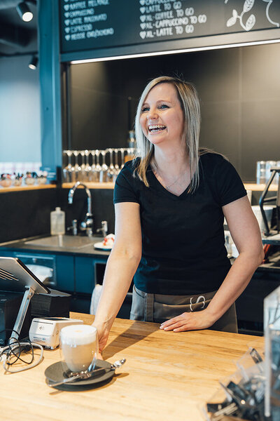 Mitarbeiterin serviert Glas mit Café Latte - Café Schnell