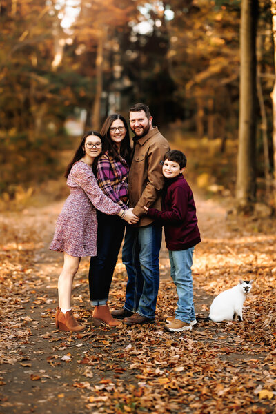 Family of four snuggles close along a path lined with fall foliage