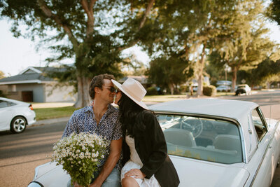 bride and groom kissing while sitting on classic car