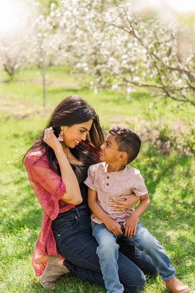 a mother sits in the grass with her son, both of them looking at each other