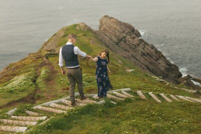 bride leads groom down trail toward a sea cliff on the East Coast Trail in Newfoundland