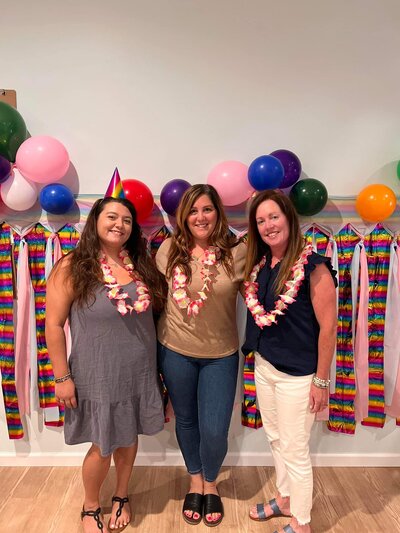 Ms. Brandi, assistant director, standing with Ms. Mia, director and Ms. Jackie, lead teacher at a luau party with accessories