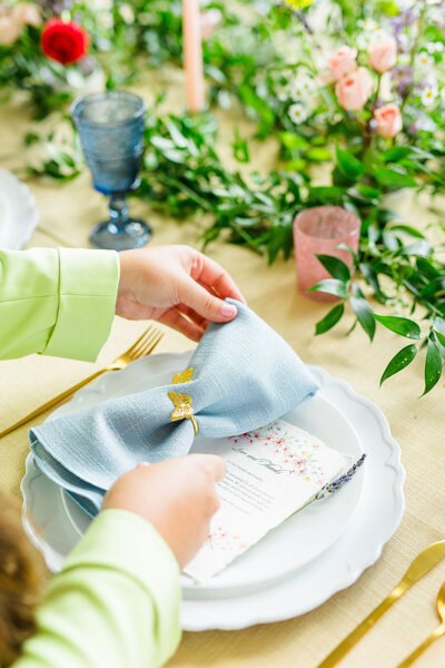 Hands placing a blue napkin on a place setting