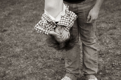 A single father holds his son upside down during their family session in their back yard.