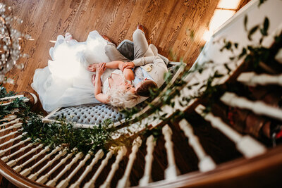 a couple sitting on a chair with the photographer looking down on them from the top of the stairs