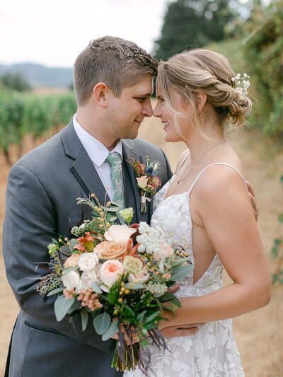 Bride and groom smile at each other and the bride holds a large bouquet representing wedding flowers designed by Eugene florist Flowers and Thyme.