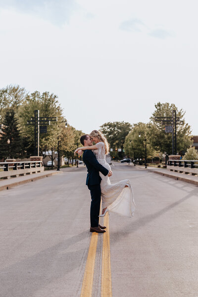 Groom lifting bride in the middle of a quiet street at golden hour, captured by a wedding photographer in Minnesota.