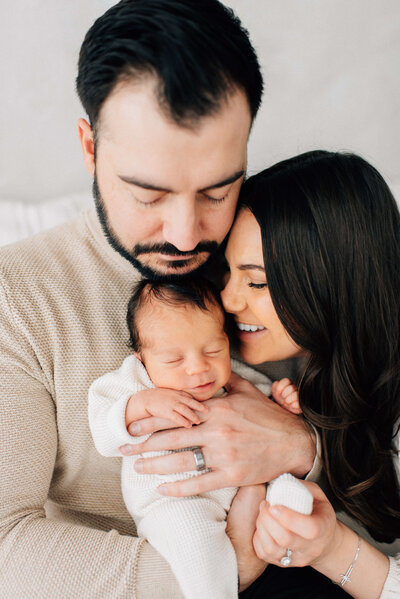 newborn baby in dad's arms while mom kisses his face and he smiles