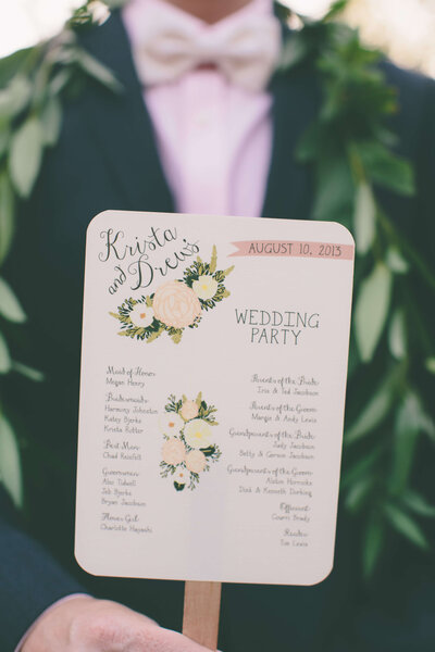 Romantic winery wedding fan style program held by the groom with hand-drawn floral details.