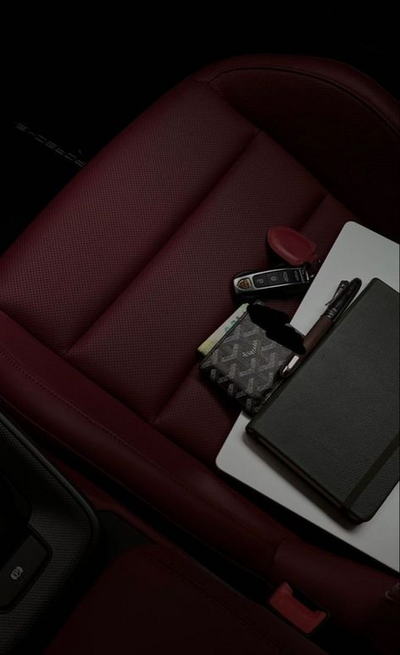 Notebook and phone placed on red leather car seat, representing freedom and luxury in business lifestyle.