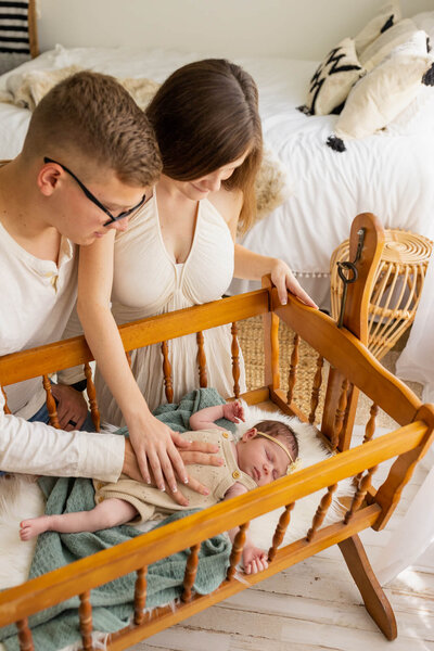 Mom and dad looking over their newborn baby laying in an antique wooden bassinet