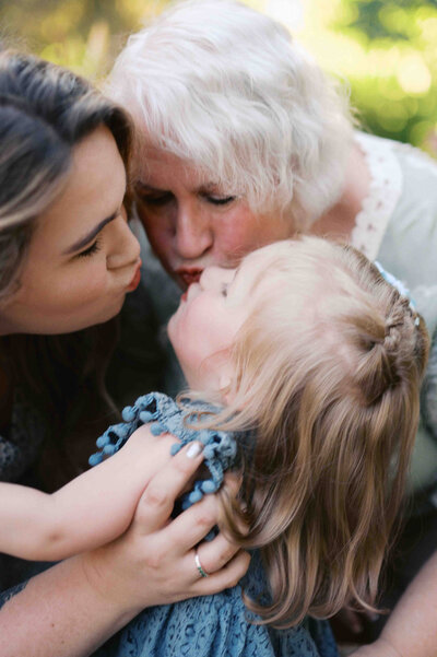 Toddler, mother, and grandmother reach in to give a group kiss with puckered lips by Portland Family Photographer Emilie Phillipson Photography. 