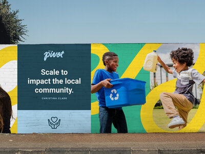 A vibrant mural on a brick wall featuring two smiling children engaged in recycling—one holding a blue bin with a recycle symbol, the other jumping with a milk jug in hand. The background includes bold, colorful shapes in yellow, green, and blue. A section of the mural features a solid blue panel with a quote and branding elements, suggesting a focus on community impact.
