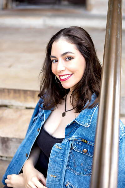 Senior girl with black hair in blue jean jack, red lipstick, and black jean dress on steps