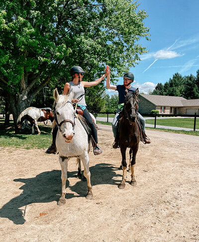 Two riders on horses sharing a high five against an Ohio backdrop.