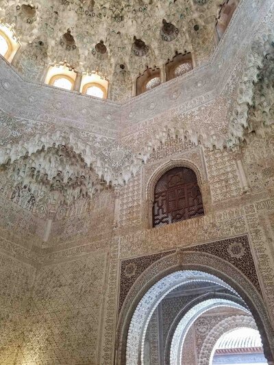 Intricate Islamic carvings and honeycomb ceiling details in the Nasrid Palaces at the Alhambra in Granada, Spain, with arched doorways framing views of connected rooms ©Stephanie Dosch | theViatrix Luxury Travel