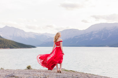 grad photo of girl standing in front of a lake with mountains in background