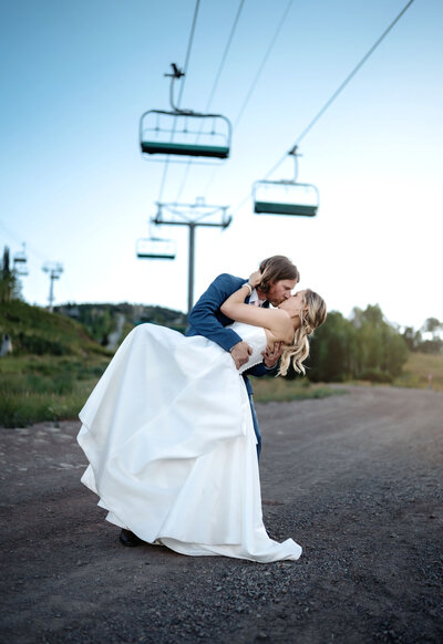 A groom dipping his bride and giving her a big kiss on the ski hills in Snowmass Colorado on their wedding day, at blue hour shot by Kelly Elizabeth Photography.