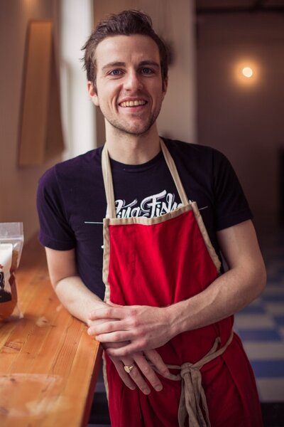 young male business owner wearing an apron smiling at the camera