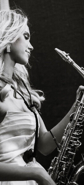 Black-and-white photo of a woman in a strapless gown playing the saxophone on stage.