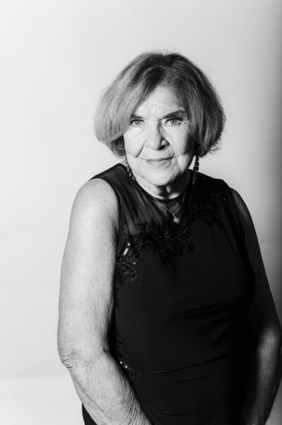 Black and white portrait of a woman wearing an elegant black evening dress with a sheer neckline, photographed on a white backdrop during a wedding reception portrait session.