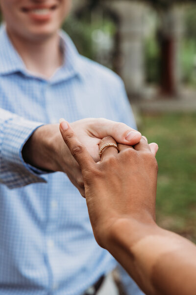 Close-up of bride-to-be’s hand with engagement ring as couple holds hands during their garden engagement session in Jacksonville