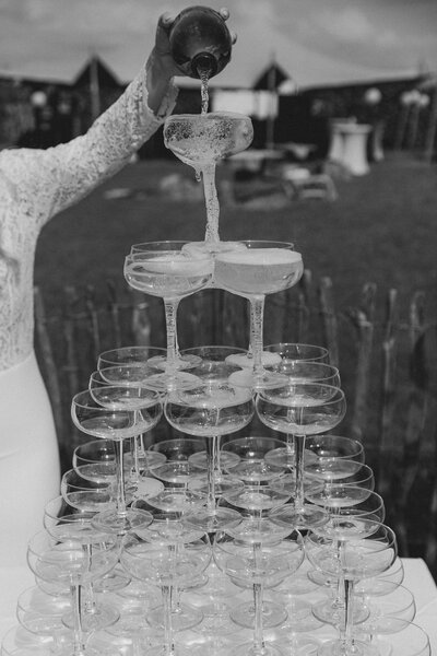 Bruid met witte jurk giet champagne in een champagnetoren op bruiloft in Nederland. 