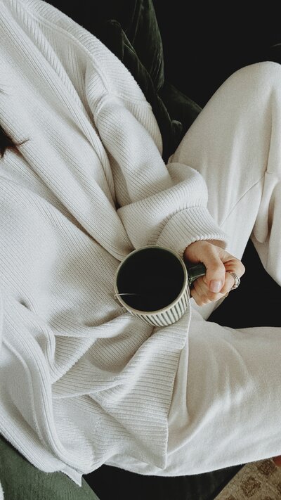 woman in white outfit holding a green and white coffee mug sitting on a green velvet chair
