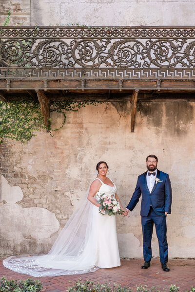 Bride and groom walking hand-in-hand along a brick sidewalk in Savannah, GA, surrounded by historic charm and greenery.
