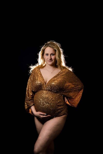 A high-key maternity photo created by Mobile, AL Maternity Photographer. The photographed mother is wearing a red dress, which compliments her skin beautifully, and is standing on a red backdrop. The train of her dress is tossed up  behind her for a modern, artistic look.