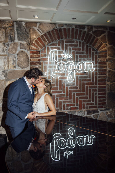 Logan Inn | Groom kissing bride under neon sign at trendy bar during wedding photo | New Hope, Pennsylvania